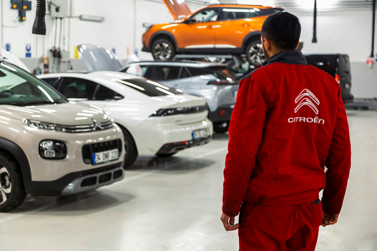 Mechaniker in roter Uniform betrachtet Autos in einer Werkstatt.
