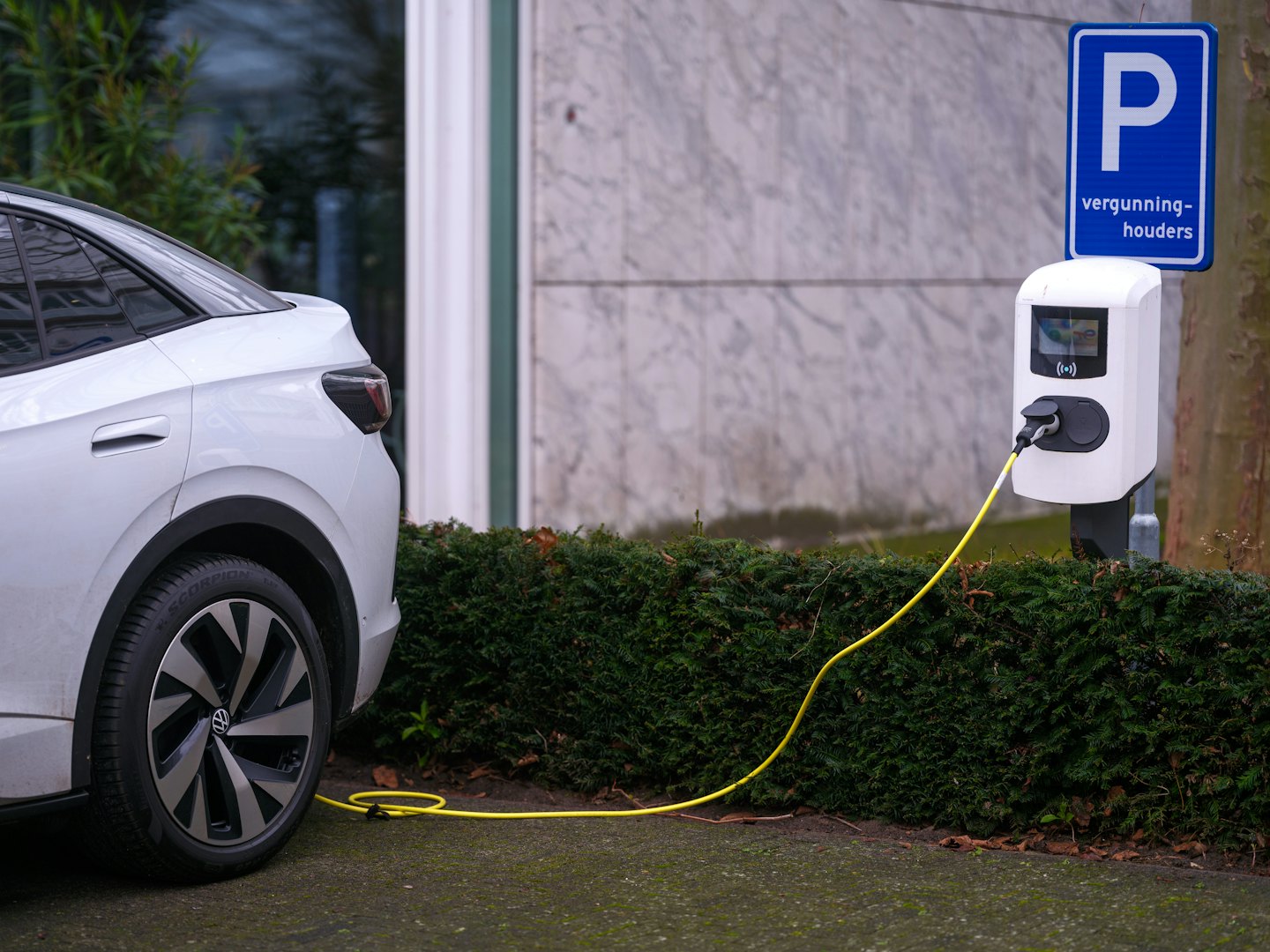 Weißes Elektroauto lädt an einer Außenstation mit gelbem Kabel.
